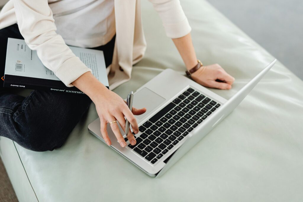 An adult using a laptop for remote work, multitasking with a book.