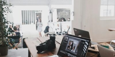 A bright, modern workspace featuring laptops, a camera, and a drawing tablet in an indoor office.