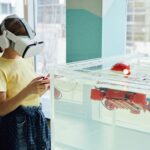 Side view of little girl wearing VR goggles and exploring new robot with controllers in light room