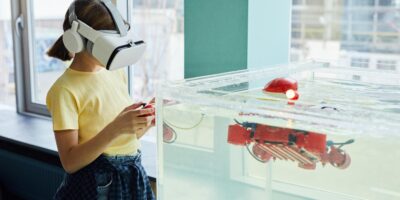 Side view of little girl wearing VR goggles and exploring new robot with controllers in light room